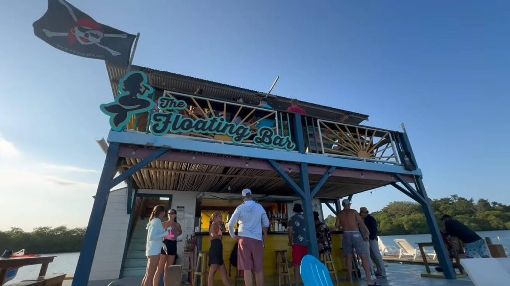 The Floating Bar" in Bocas del Toro, Panama, featuring a tropical wooden structure, blue water, and travelers relaxing on a sunny day.
